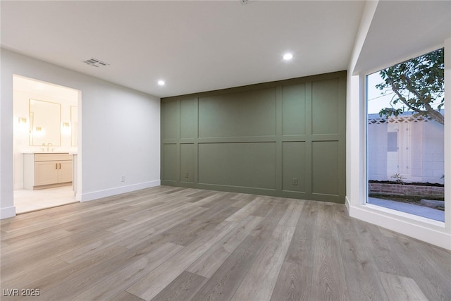 empty room with light wood-style flooring, a decorative wall, a sink, and recessed lighting