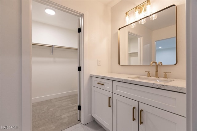 bathroom with vanity, baseboards, and a spacious closet