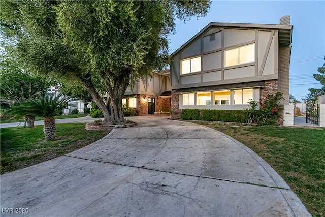 tudor home featuring a front yard, a chimney, stucco siding, brick siding, and curved driveway