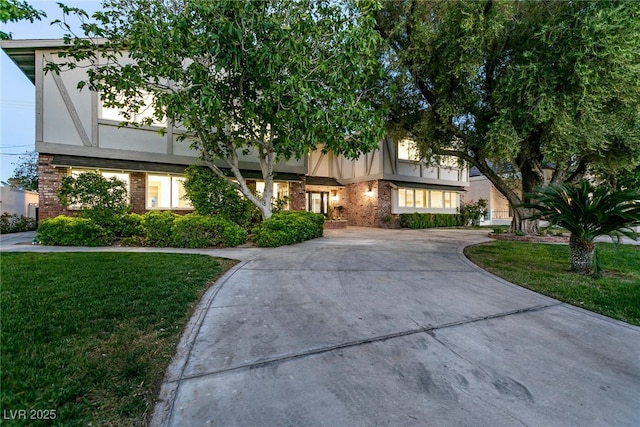 view of front of property featuring brick siding, a front lawn, curved driveway, and stucco siding
