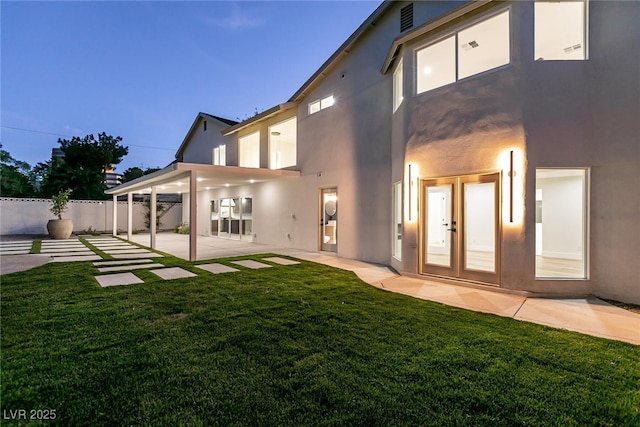 rear view of house featuring a yard, fence, a patio, and stucco siding