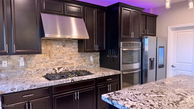 kitchen with under cabinet range hood, appliances with stainless steel finishes, decorative backsplash, light stone countertops, and dark brown cabinets