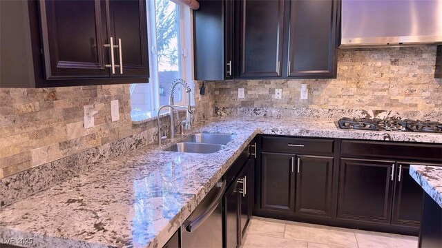 kitchen with a sink, stainless steel appliances, wall chimney exhaust hood, light stone counters, and backsplash
