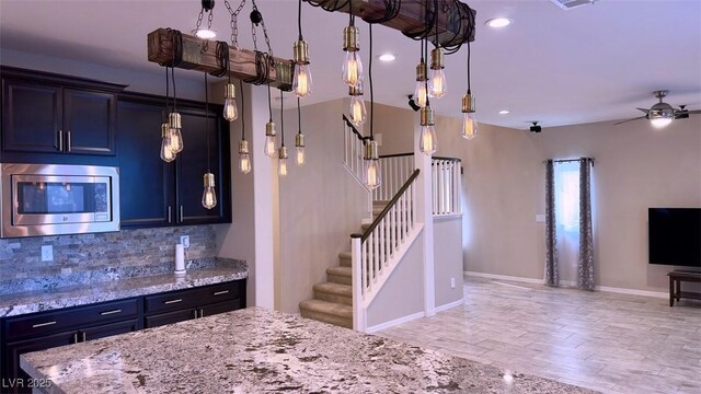kitchen with stainless steel microwave, backsplash, light stone counters, open floor plan, and baseboards