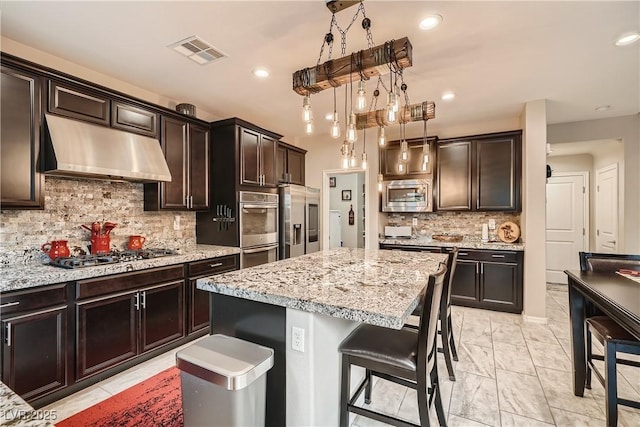 kitchen with range hood, stainless steel appliances, a breakfast bar area, light stone counters, and decorative backsplash