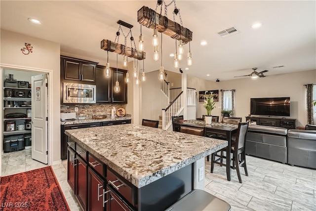 kitchen featuring stainless steel microwave, open floor plan, ceiling fan, light stone counters, and decorative backsplash