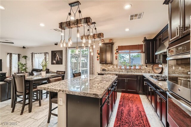 kitchen featuring tasteful backsplash, stainless steel appliances, light stone counters, open floor plan, and a center island
