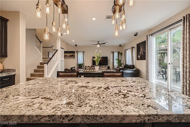 kitchen with light stone counters, open floor plan, a ceiling fan, a kitchen island, and pendant lighting