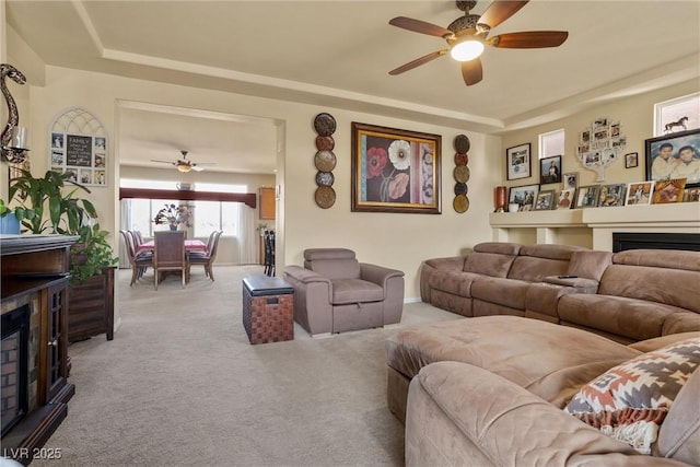 carpeted living room with a fireplace, a tray ceiling, and ceiling fan