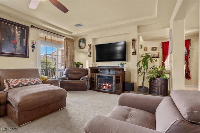 carpeted living area with visible vents, a ceiling fan, and a glass covered fireplace
