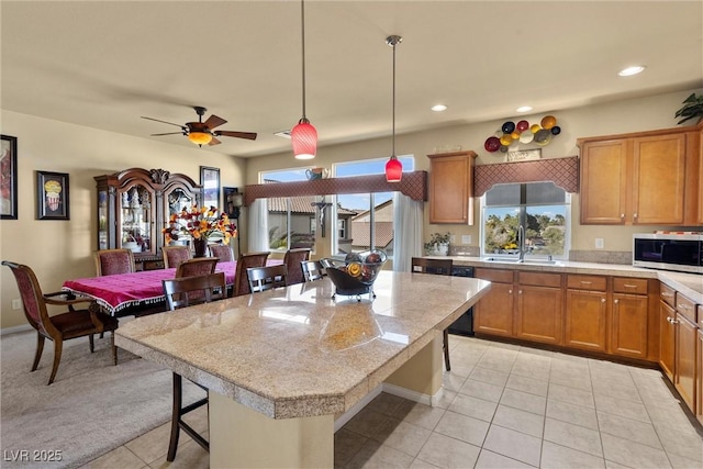kitchen with light countertops, stainless steel microwave, a kitchen breakfast bar, and brown cabinetry
