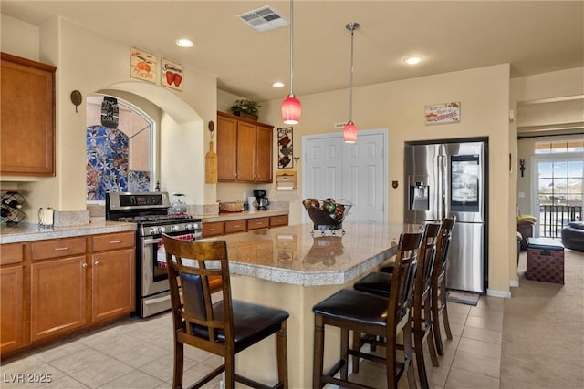 kitchen featuring light tile patterned floors, brown cabinetry, a kitchen breakfast bar, and stainless steel appliances