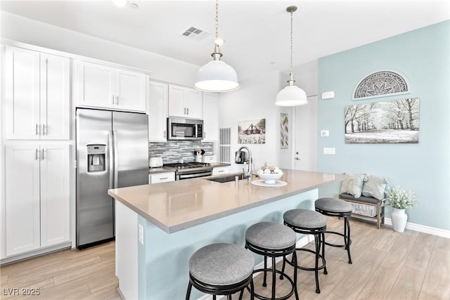 916 Belleforte Ln, Las Vegas, NV 89138 - kitchen featuring appliances with stainless steel finishes, tasteful backsplash, light wood-style floors, white cabinets, and a kitchen breakfast bar
