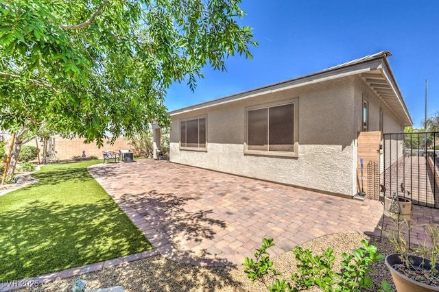rear view of property with a patio area, stucco siding, fence, and a lawn