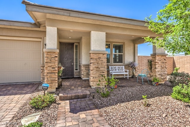 view of exterior entry with a porch, a garage, stucco siding, and stone siding