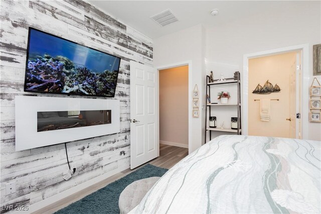 bedroom with baseboards, visible vents, wood finished floors, and an accent wall