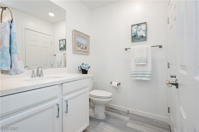bathroom with vanity, wood finished floors, toilet, baseboards, and recessed lighting