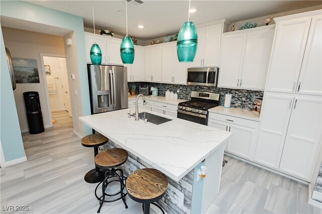 kitchen with a breakfast bar area, white cabinets, tasteful backsplash, a sink, and appliances with stainless steel finishes