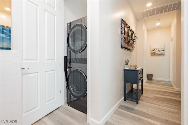 clothes washing area featuring laundry area, stacked washer and clothes dryer, visible vents, baseboards, and light wood-type flooring