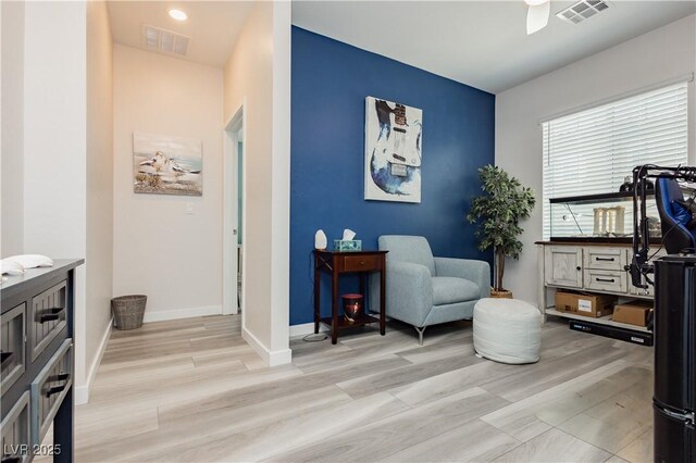 living area featuring baseboards, a ceiling fan, light wood-type flooring, and visible vents