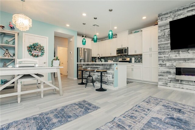 kitchen with appliances with stainless steel finishes, a breakfast bar, a kitchen island with sink, white cabinetry, and visible vents