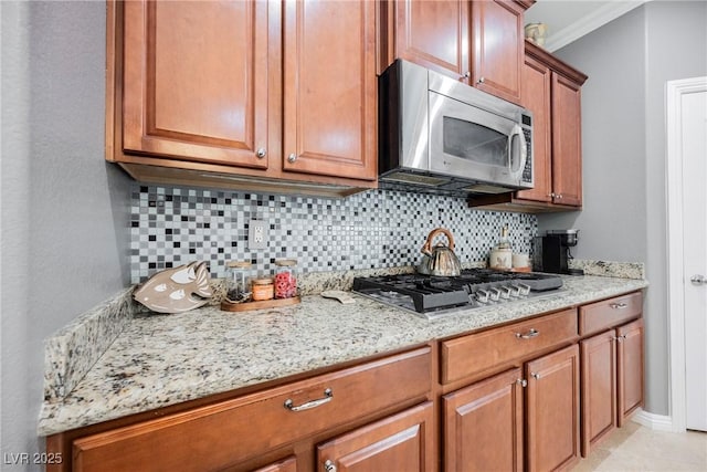 kitchen featuring crown molding, brown cabinetry, decorative backsplash, stainless steel appliances, and light stone countertops