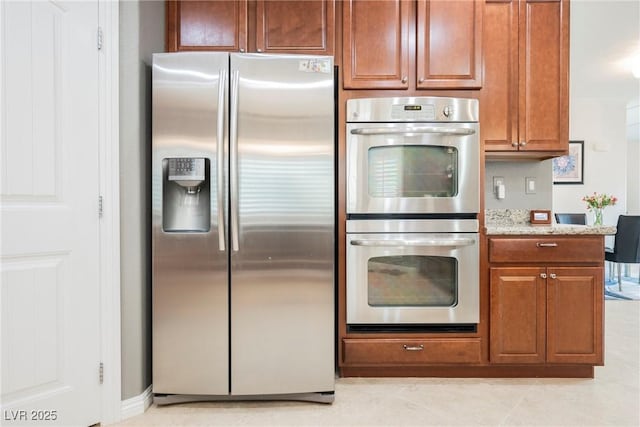 kitchen featuring brown cabinetry, appliances with stainless steel finishes, and light stone counters