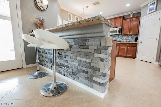 bar featuring stainless steel microwave, backsplash, visible vents, and light tile patterned floors