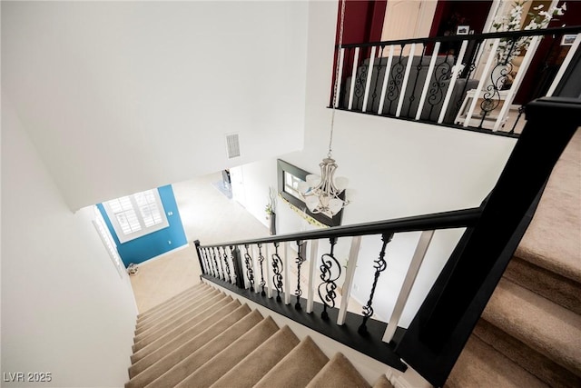 stairway featuring a notable chandelier, a towering ceiling, visible vents, and carpet