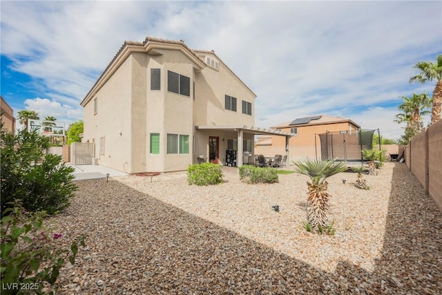 rear view of property featuring a gate, a fenced backyard, stucco siding, a patio, and a trampoline