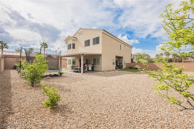 rear view of property with stucco siding, a patio area, a fenced backyard, and a trampoline