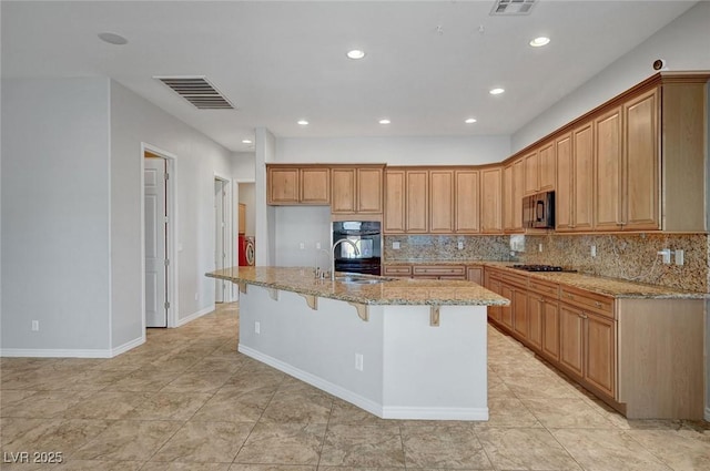 kitchen featuring light stone countertops, a sink, an island with sink, visible vents, and black appliances