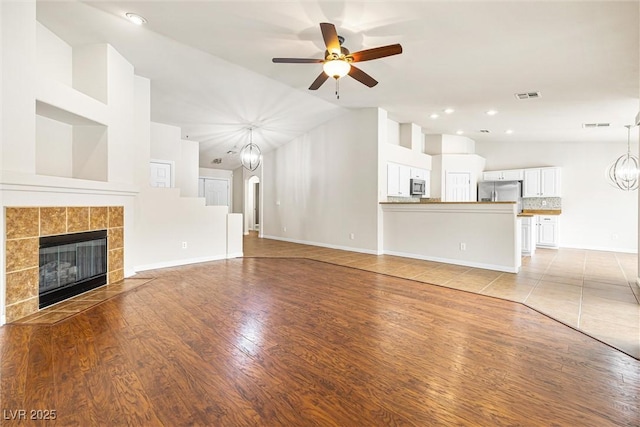 9539 Iris Flat Ct, Las Vegas, NV 89178 - unfurnished living room featuring a chandelier, ceiling fan, a tile fireplace, light wood-style floors, and baseboards