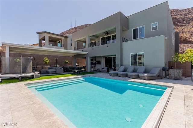 back of property with a trampoline, a balcony, a patio, an outdoor living space, and a fenced in pool