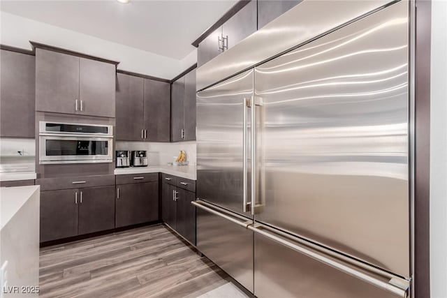 kitchen with stainless steel appliances, dark brown cabinetry, light countertops, and light wood-type flooring