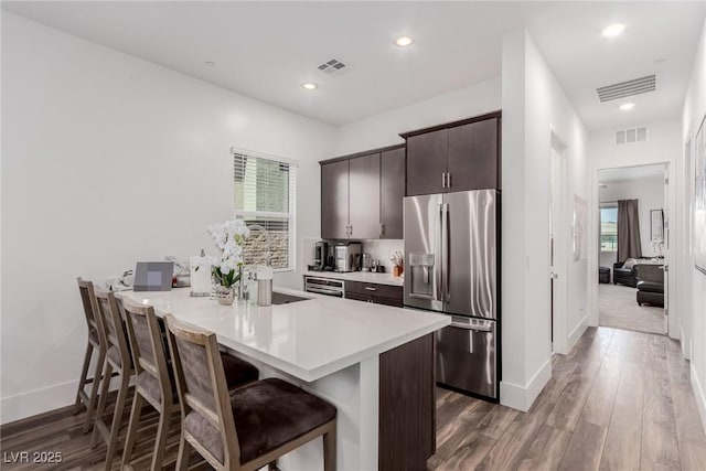 kitchen with baseboards, a breakfast bar area, dark brown cabinetry, light countertops, and stainless steel fridge with ice dispenser