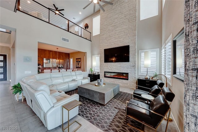 tiled living area featuring visible vents, a fireplace, a towering ceiling, and ceiling fan with notable chandelier