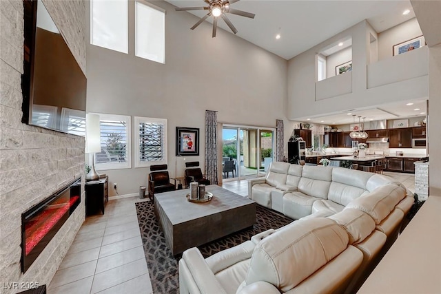 living area with a glass covered fireplace, baseboards, a high ceiling, a ceiling fan, and light tile patterned flooring
