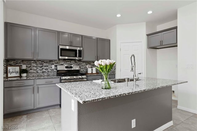 5317 Golden Melody Ln, North Las Vegas, NV 89081 - kitchen with stainless steel appliances, light stone countertops, backsplash, a kitchen island with sink, and gray cabinets