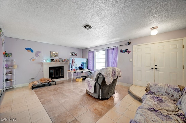 living area featuring visible vents, a glass covered fireplace, light tile patterned floors, and a textured ceiling