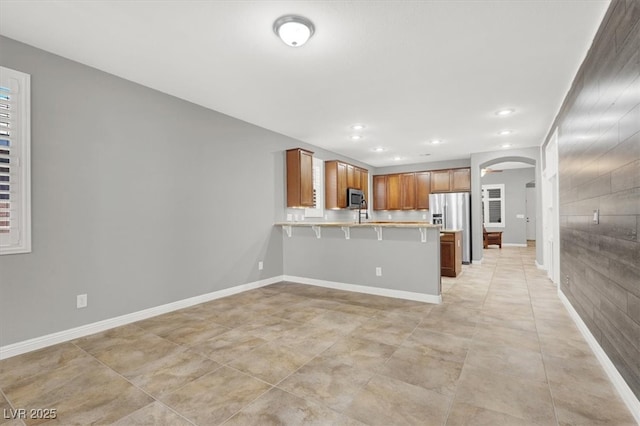 7806 Sundial Peak St, Las Vegas, NV 89166 - kitchen featuring appliances with stainless steel finishes, a peninsula, light countertops, a kitchen bar, and arched walkways