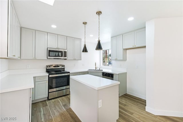 kitchen with a sink, light wood-type flooring, decorative light fixtures, a kitchen island, and appliances with stainless steel finishes