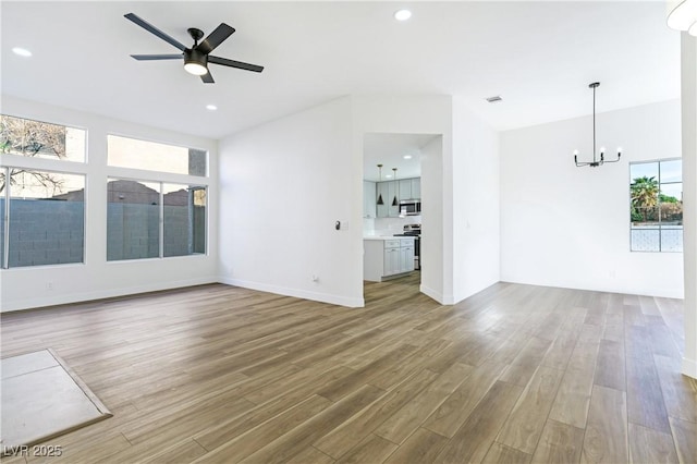 unfurnished living room featuring ceiling fan with notable chandelier, wood finished floors, and recessed lighting