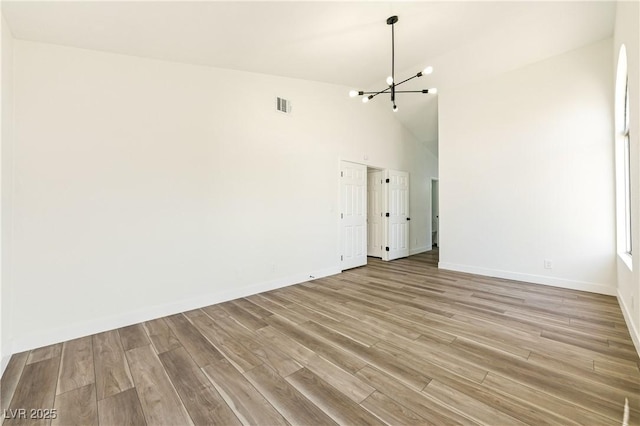 unfurnished living room featuring visible vents, baseboards, a chandelier, light wood finished floors, and high vaulted ceiling