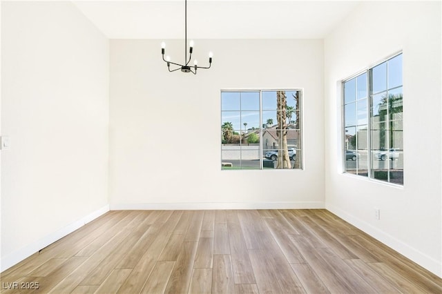empty room featuring light wood-style floors, baseboards, and an inviting chandelier