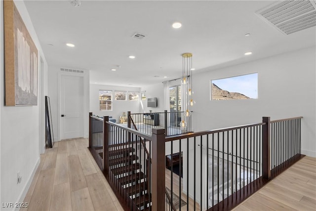 hallway with visible vents, an upstairs landing, and light wood finished floors