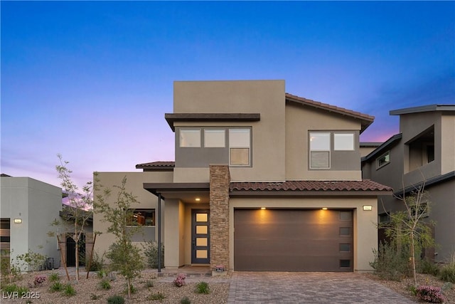contemporary home featuring a tiled roof, decorative driveway, a garage, and stucco siding