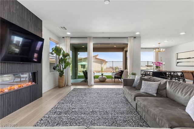living room featuring a large fireplace, visible vents, a chandelier, wood finished floors, and baseboards