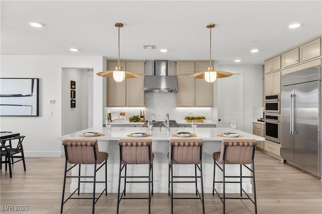 kitchen featuring visible vents, wall chimney exhaust hood, light countertops, appliances with stainless steel finishes, and light wood finished floors