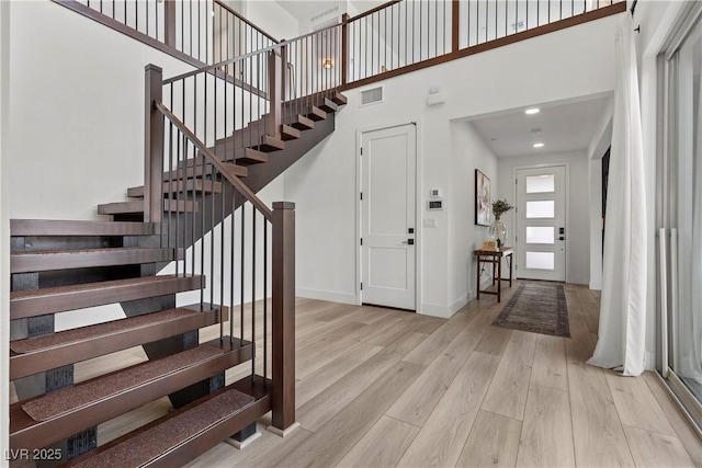 stairs featuring visible vents, baseboards, a towering ceiling, and wood finished floors